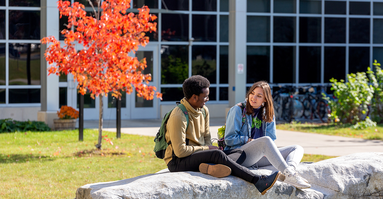Two students sit on a boulder on campus