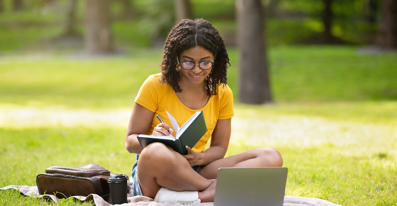 female student studying outside in the grass with her laptop and notebook