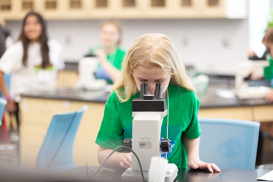 girl looking into microscope at STEM program
