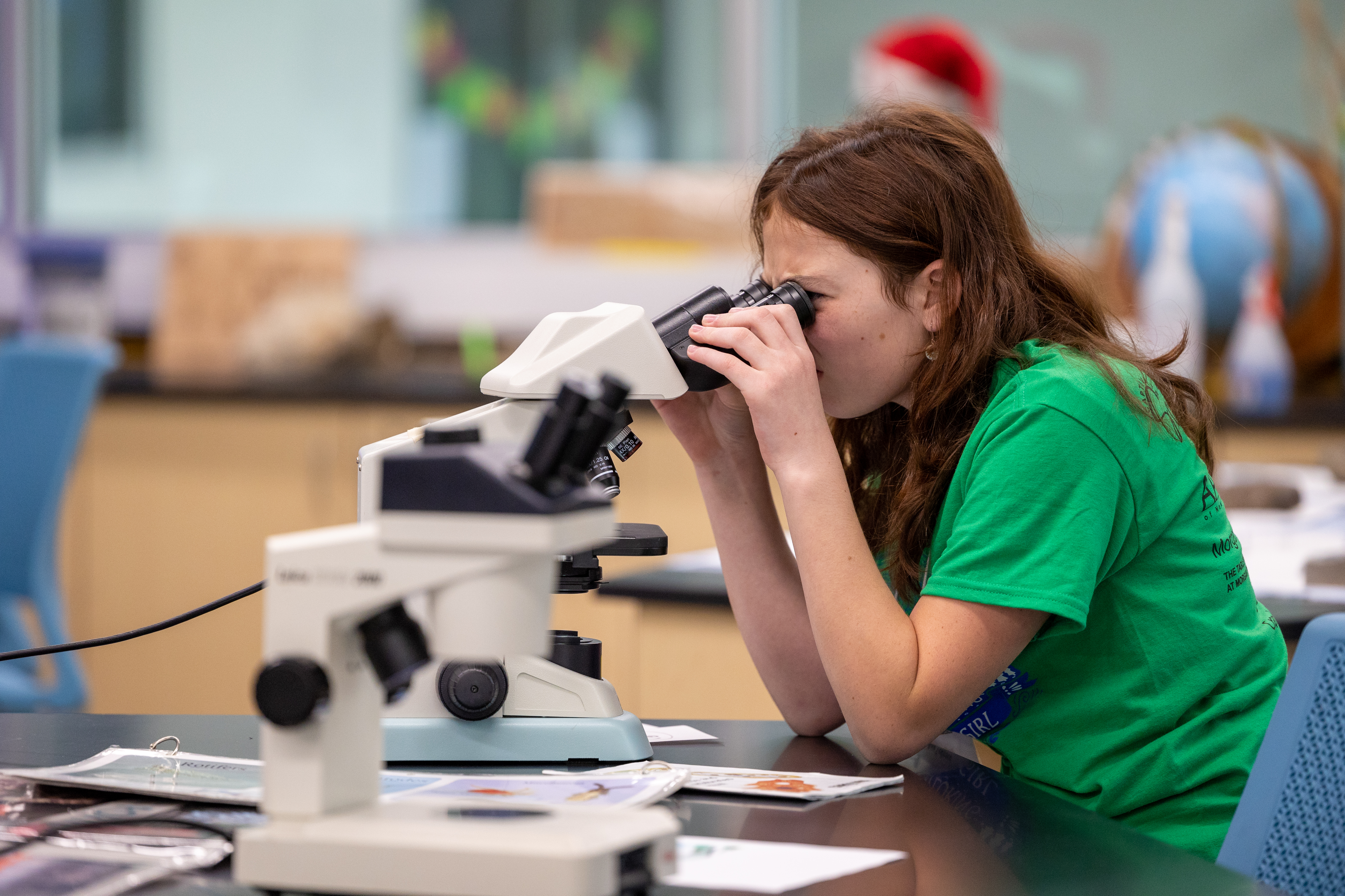 A young teenage girls looks into the eyepieces of a microscope in a labratory