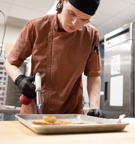 A Culinary student torches scallops in the kitchen of Seasoned