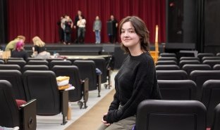 Mary Pilot of Hoosick Falls poses for a photo in the theater, while the cast of "The Addams Family" rehearses in the background.