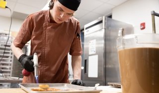 A student torches a dish in preparation of a fine dining experience at Seasoned