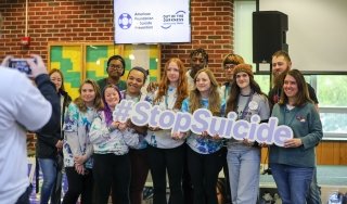 A group of students and faculty hold up a #stopsuicide sign to advocate for awareness