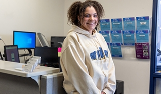 Sophia Goldsmith smiles at the camera in the Student Activities office. She has dark curly hair and wears a hooded sweatshirt.