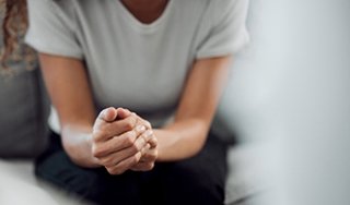 Stock image of a person's hands, as they lean forward, appearing to be in an intimate discussion