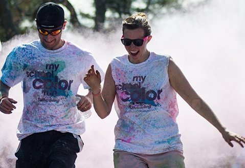 Two friends laugh and celebrate finishing a color run on the SUNY Adirondack campus