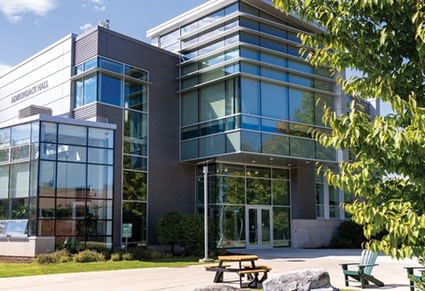 Image of Adirondack Hall in the summer with a blue sky and picnic table in the foreground