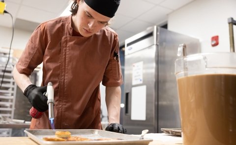 A student torches a dish in preparation of a fine dining experience at Seasoned