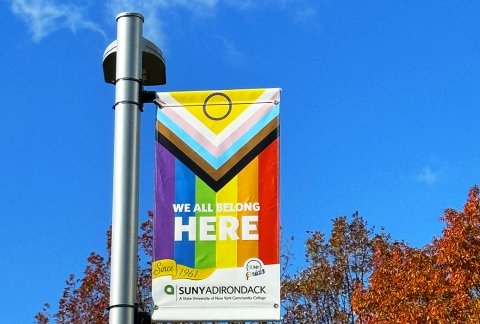 A pride flag with a "We all belong here" message flies on campus