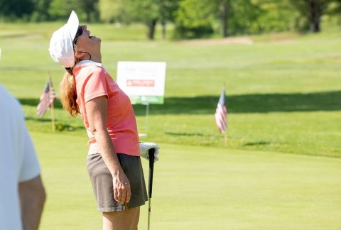 A woman wearing a coral-colored golf shirt and white visor throws her head back in laughter during the 2021 event