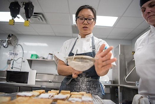 A student sifts confectioner's sugar onto a dessert at Seasoned.