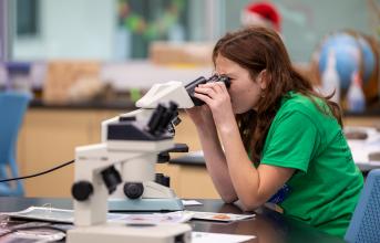 A young teenage girls looks into the eyepieces of a microscope in a labratory