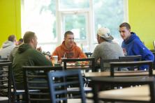 A group of young men talk while sitting at a dining hall table.